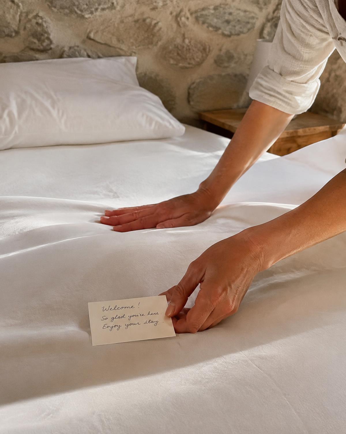 Manos preparando la cama con una nota de bienvenida
